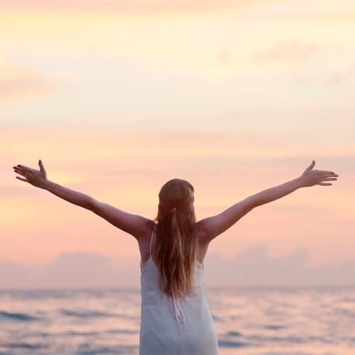 Woman stood looking out to the sea with her arms out